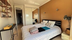 A bedroom with a bed, bedside tables, a mirror, and a door leading to another room. - Beautiful 2 bedroom terrace and parking (Cannes)