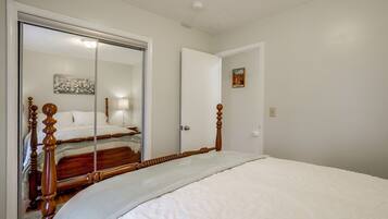 A bedroom with a large mirror, a bed with wooden headboard, a door, and a wall-mounted light fixture.
