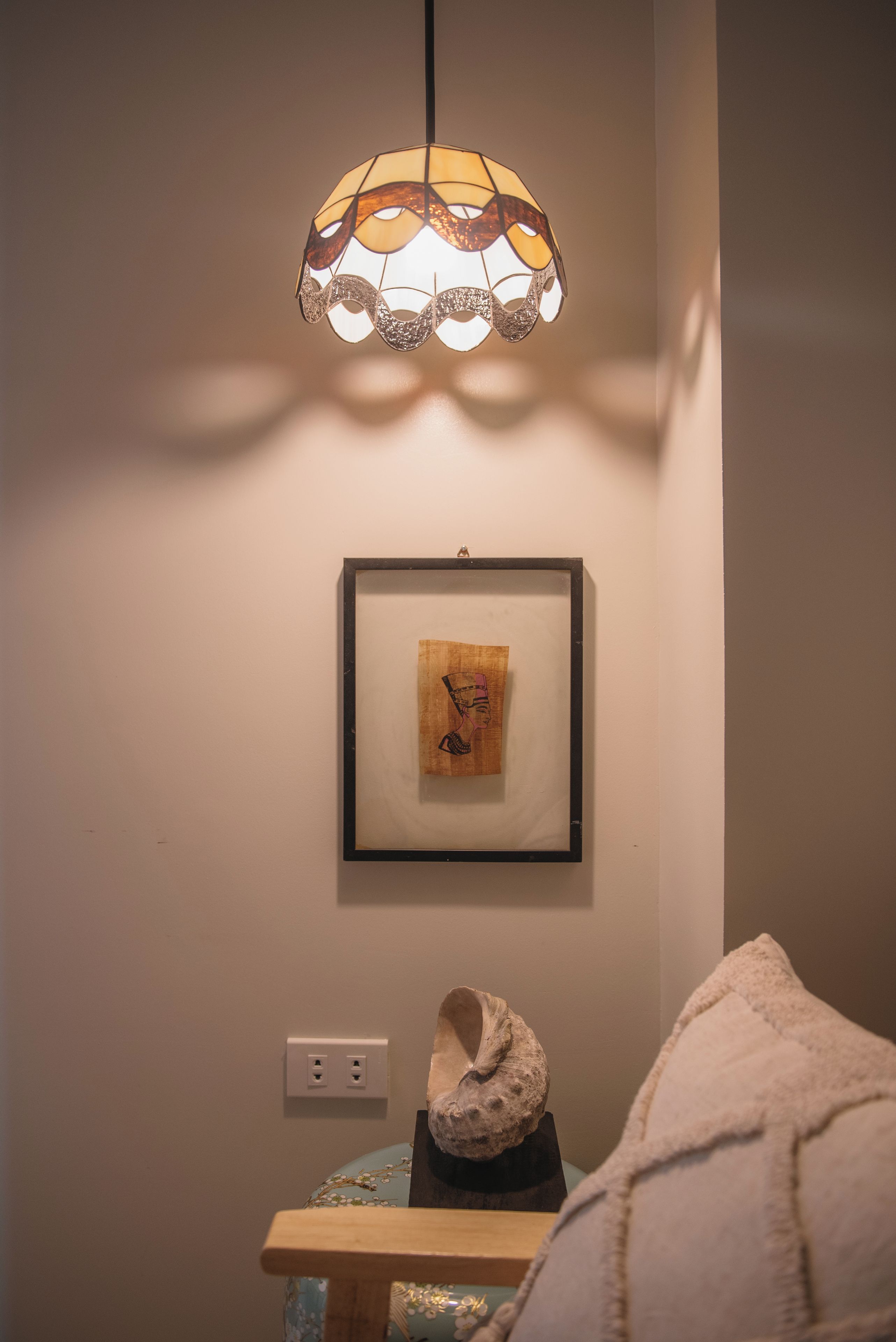 Een kamer met een gekaderd kunstwerk aan de muur, een tafel met een decoratief object en een hanglamp.