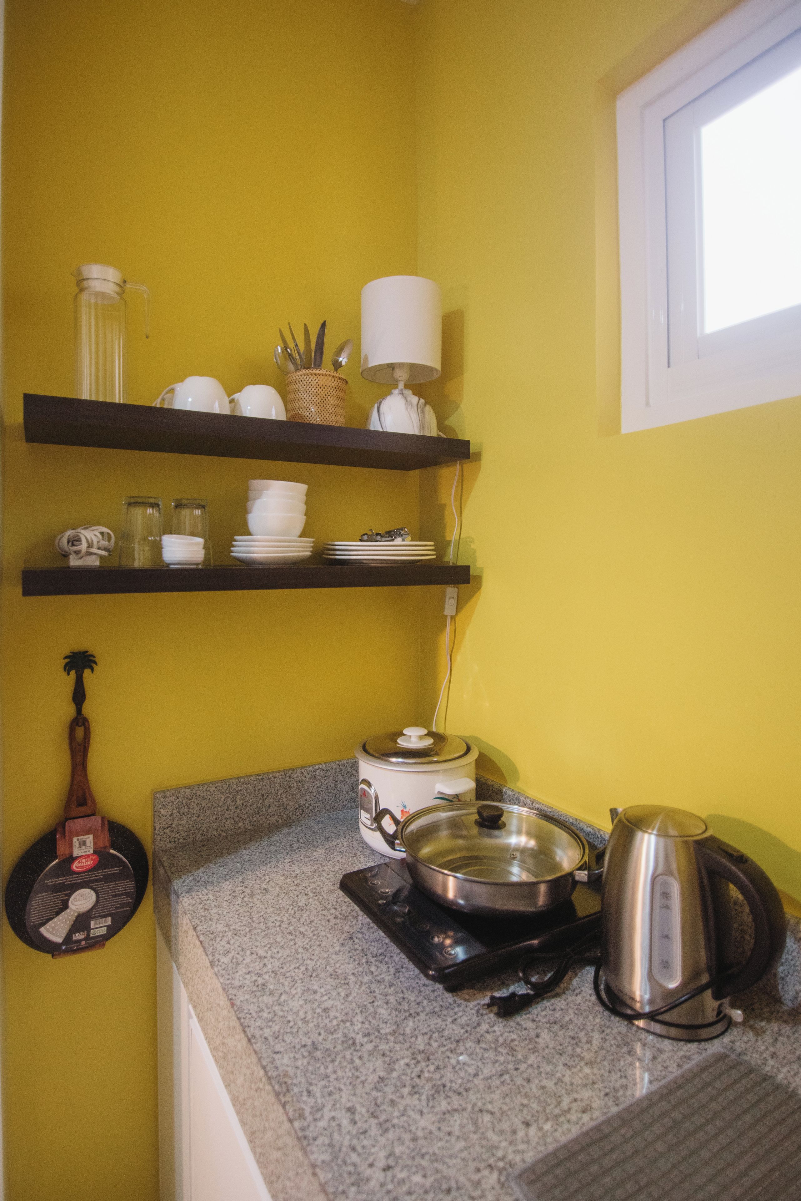 A kitchen with yellow walls, a granite countertop, a stove, a kettle, and shelves with dishes and utensils.