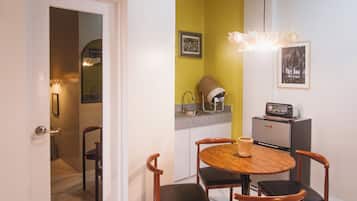 Un espacio comedor compacto con una mesa redonda, cuatro sillas y una pequeña zona de cocina con refrigerador y microondas.
