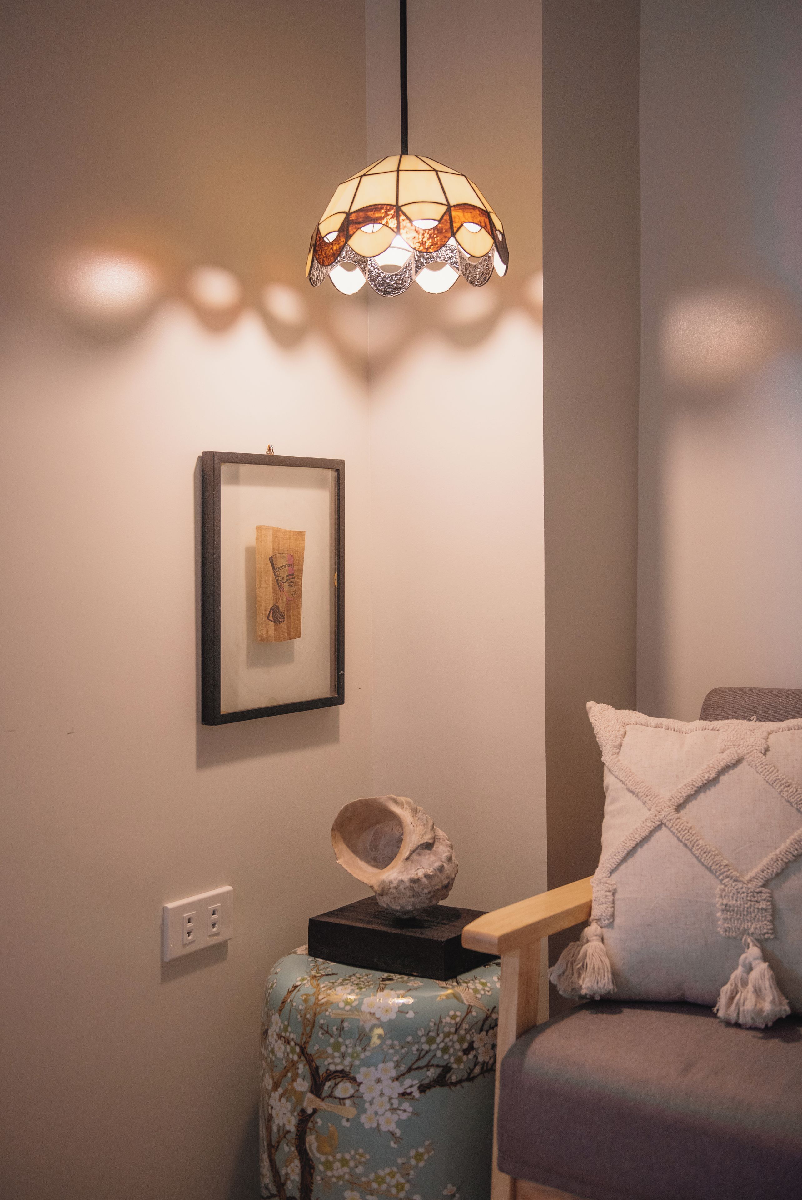 Una habitación con un cuadro en la pared, una lámpara decorativa, una pequeña escultura en un pedestal y un sillón acolchado.