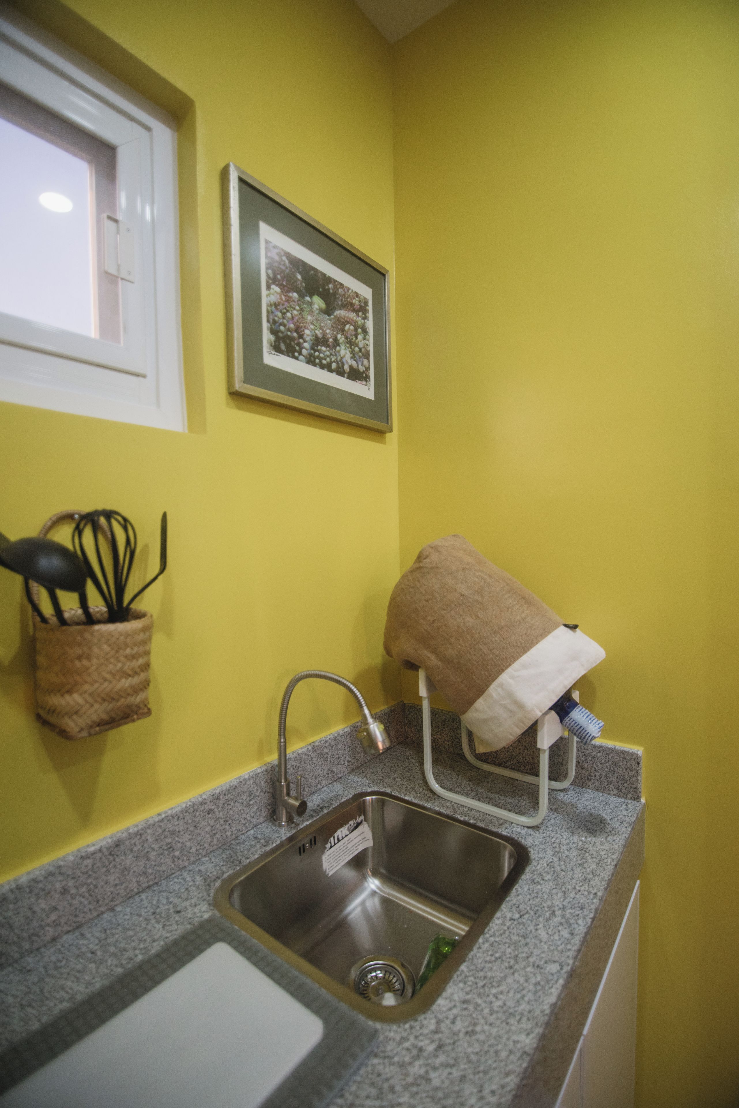 Una cocina con un lavamanos de acero inoxidable, una ventana y un cuadro en la pared.