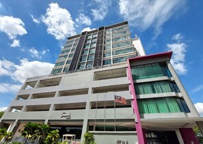 A multi-story building with a prominent flag, a sign indicating a business or hotel, and a clear sky. - 591 DSA by Hostech.ai (Shah Alam)