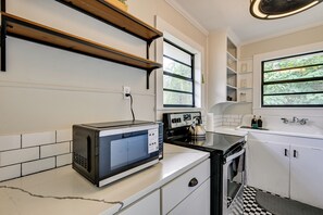 A kitchen with a microwave, stove, and sink. There is a window with a view of greenery outside. - 1BR Tampa Apt, Close to Downtown (Tampa)