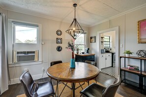 Uma sala de jantar com mesa redonda de madeira, cadeiras de couro preto, luminária pendente e uma janela com ar condicionado.