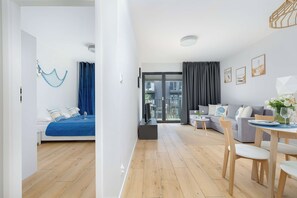 A modern living room with a sofa, a dining table with chairs, a TV, and a balcony with a view.