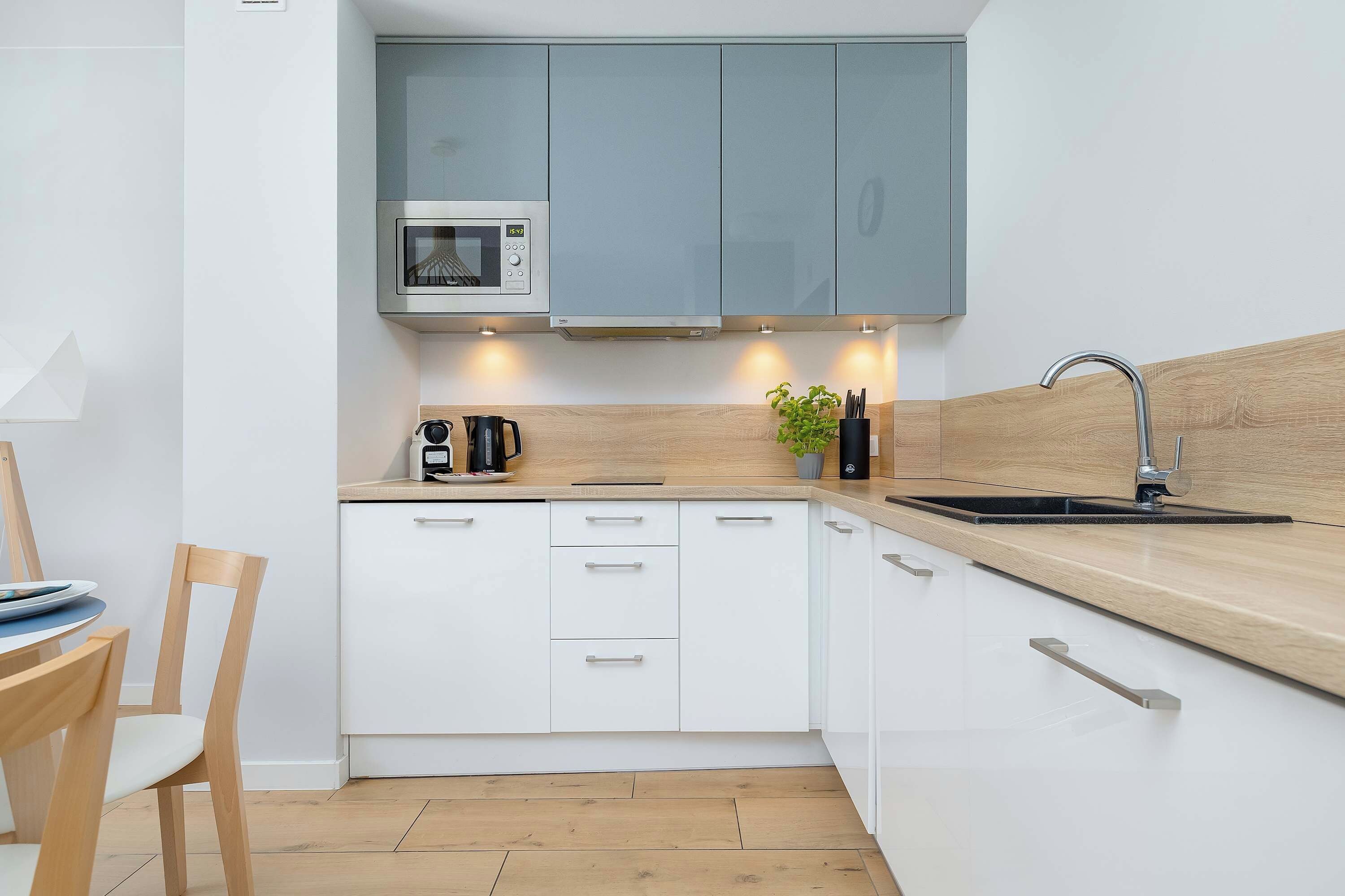 Una cocina compacta con armarios blancos, microondas, cafetera y lavamanos.