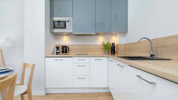 Una cocina compacta con armarios blancos, microondas, cafetera y lavamanos.