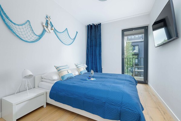 A bedroom with a large bed, white nightstand, and a TV mounted on the wall.