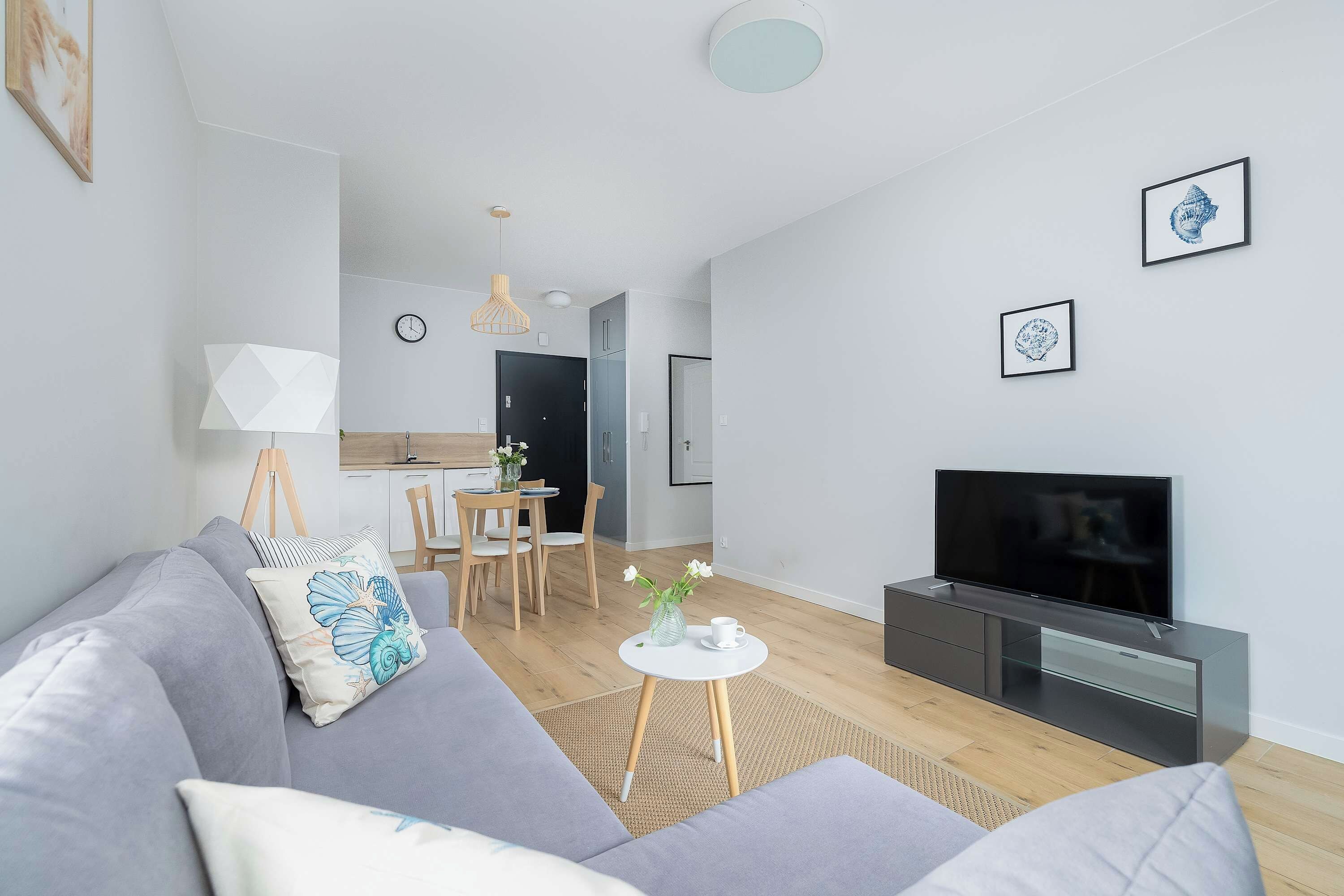 Una sala de estar moderna con un sofá gris, un televisor de pantalla plana y un comedor con sillas de madera y una mesa pequeña.