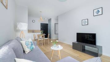 Una sala de estar moderna con un sofá gris, un televisor de pantalla plana y un comedor con sillas de madera y una mesa pequeña.