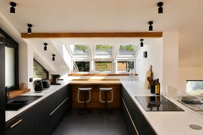 A modern kitchen with a central island, bar stools, and a view through large windows. - Chalet Bois du Lac 8p/4r (Chamonix-Mont-Blanc)