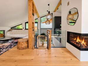 A modern living room with a fireplace, wooden accents, and a large window. - Chalet Bois du Lac 8p/4r (Chamonix-Mont-Blanc)
