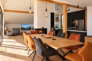 Una sala de estar moderna con una gran mesa de comedor de madera, asientos cómodos, una chimenea y una cocina equipada con electrodomésticos modernos.