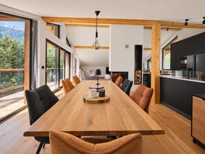 A modern dining area with a long wooden table, multiple chairs, and a view of the outdoors. - Chalet Bois du Lac 8p/4r (Chamonix-Mont-Blanc)