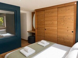 Un dormitorio moderno con una cama, dos toallas enrolladas, un armario de madera, un espejo y una ventana.