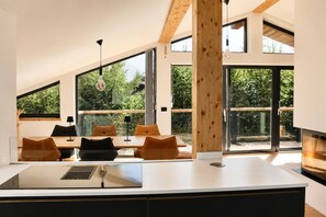 Una cocina moderna con una isla grande, vigas de madera y ventanas amplias con vistas a follaje.