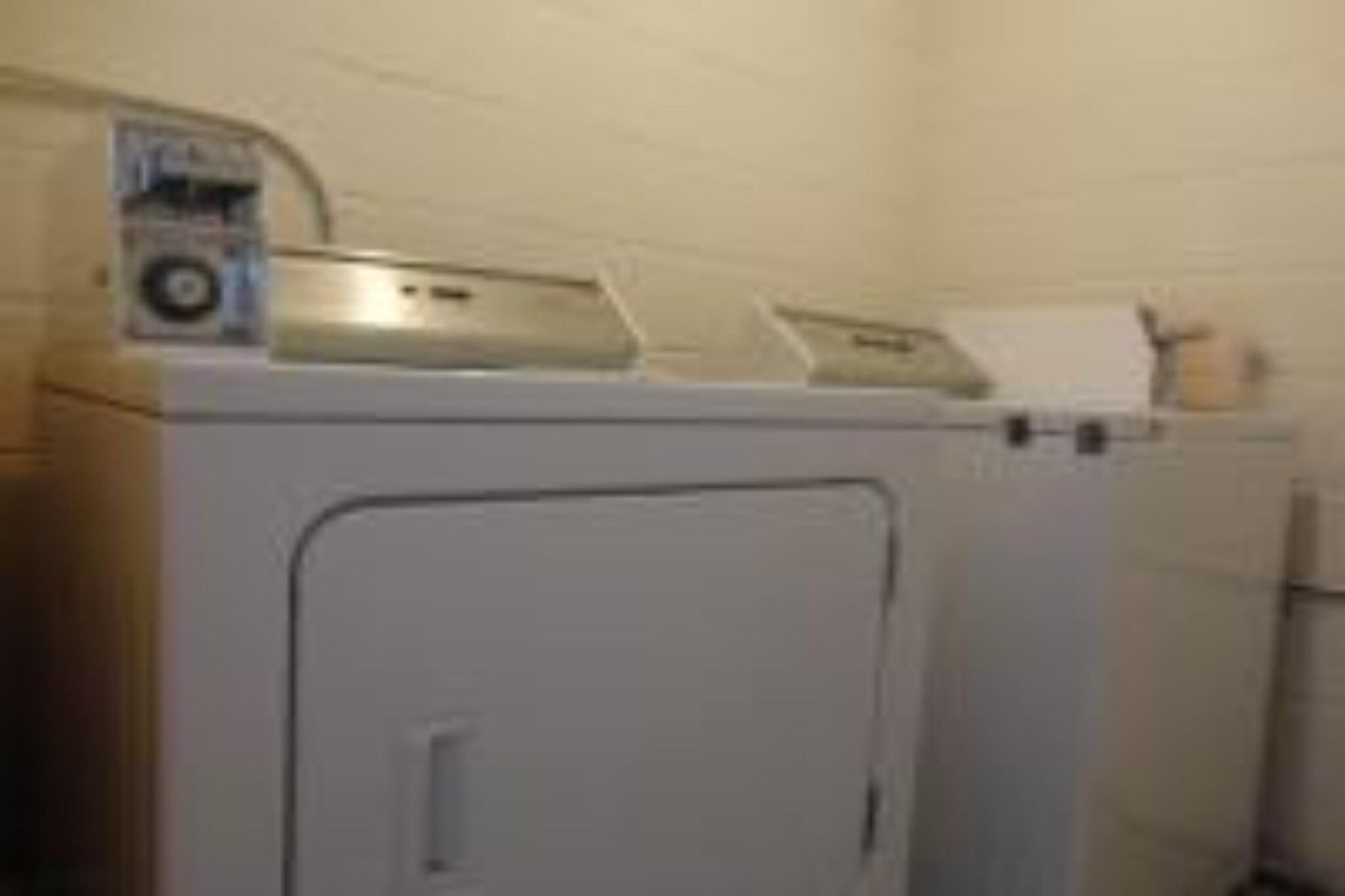 A compact, white laundry machine with a control panel and a paper towel dispenser on top.