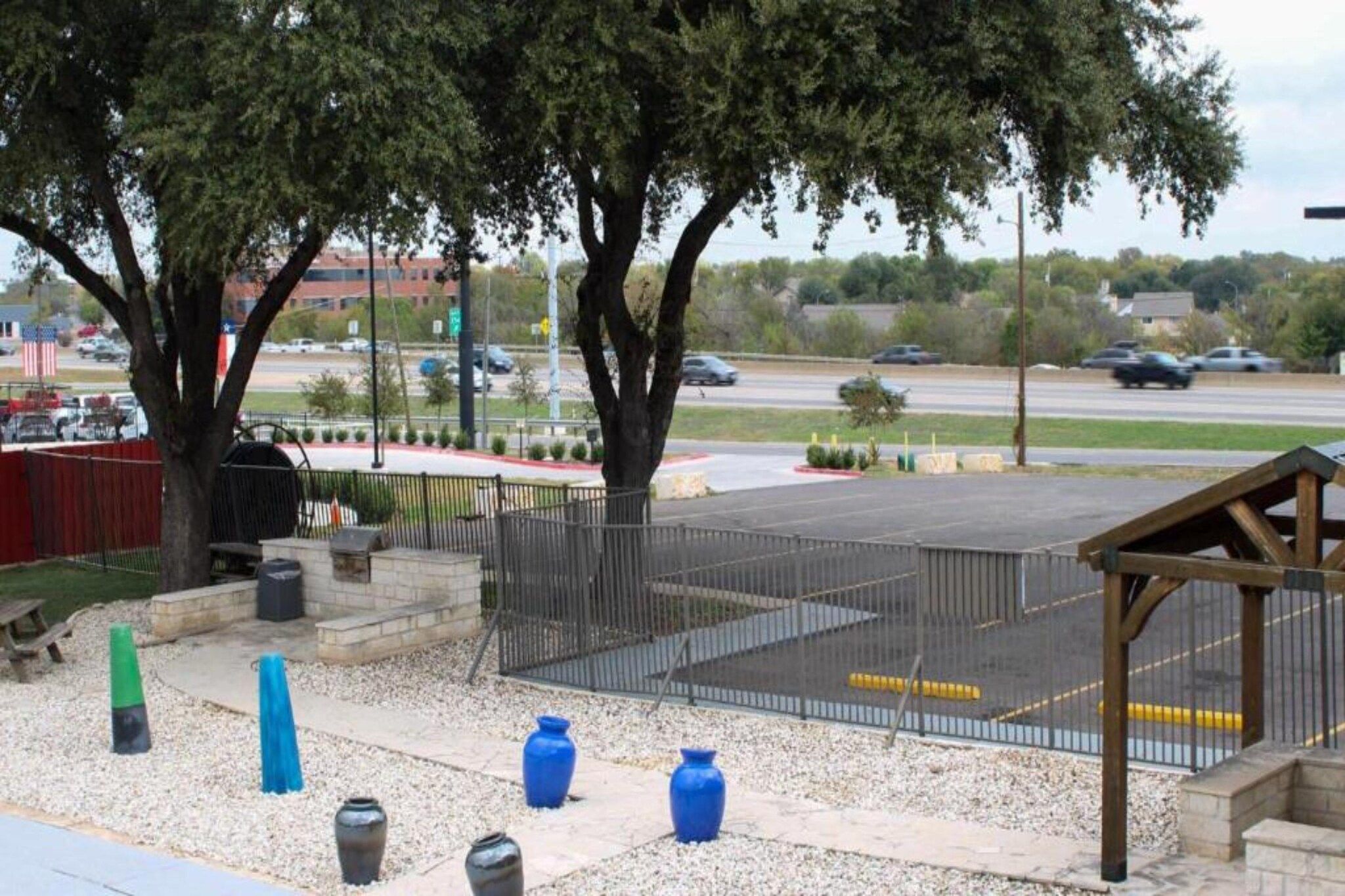 An outdoor area with a fenced sports court, trees, and a parking lot in the background.