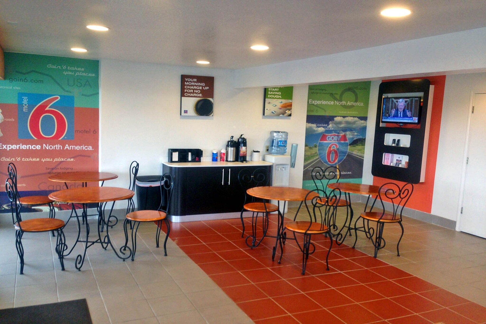 A lobby with a reception desk, several tables and chairs, and promotional posters on the walls.