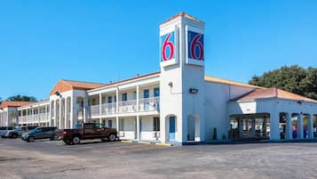 A motel with a central tower featuring the number '6', a parking lot, and a building with a red roof.