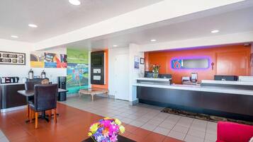 A hotel lobby with a reception desk, a seating area with a coffee machine, and a colorful wall mural.