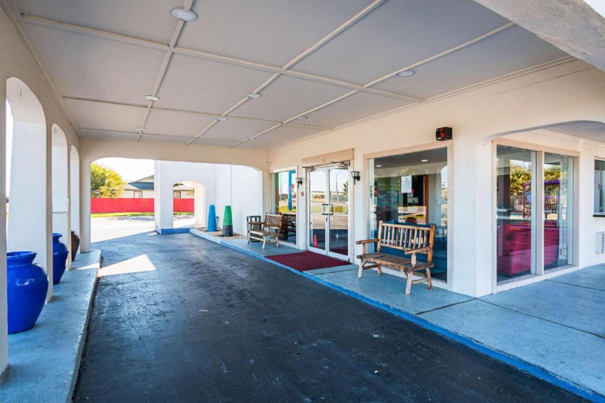 A covered outdoor area with a bench, a red carpet, and a glass door entrance.