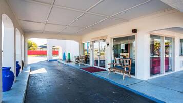 A covered outdoor area with a bench, a red carpet, and a glass door entrance.