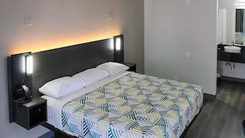 A hotel room with a bed, bedside table, and a bathroom with a sink and mirror.