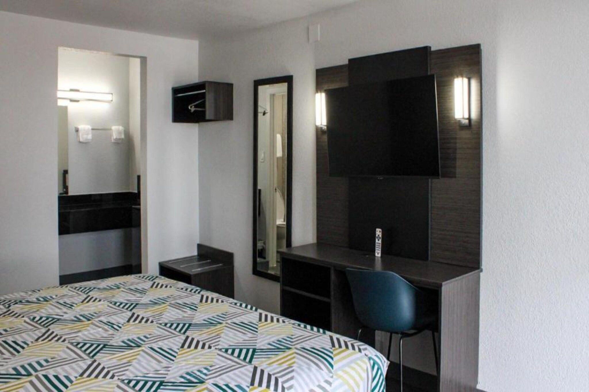 Une chambre d’hôtel équipée d’un lit, d’un bureau, d’une chaise, d’un miroir et d’une télévision.