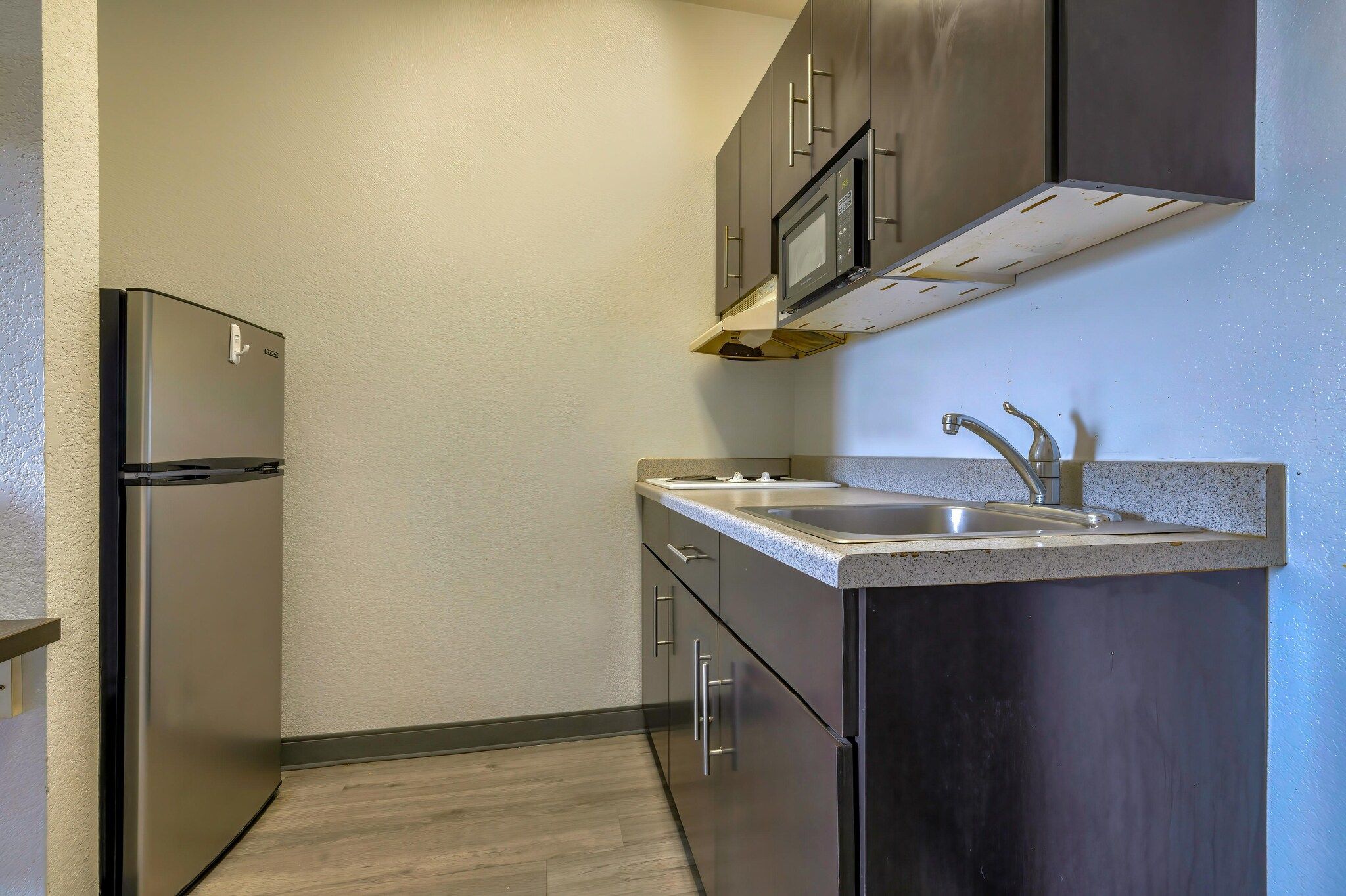 A kitchen with a stainless steel refrigerator, a sink with a modern faucet, and dark cabinetry.