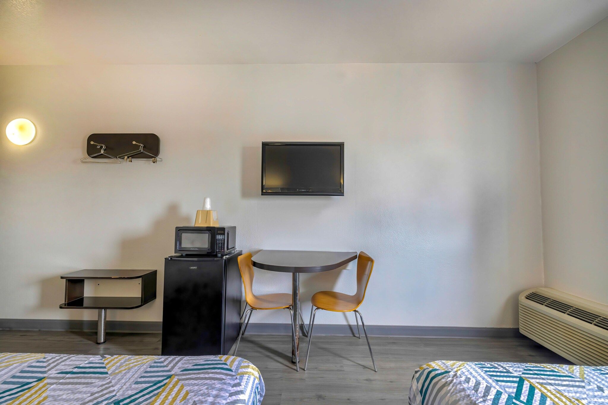 Una habitación pequeña con dos camas, una mesa con sillas, microondas, televisión y calefacción.