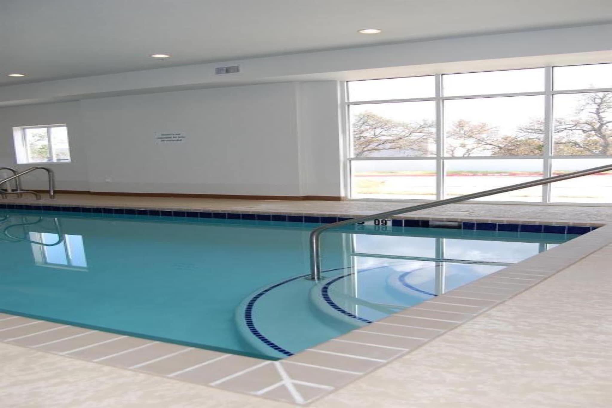 Una piscina interior con agua cristalina, una terraza de baldosas y vistas al exterior a través de amplias ventanas.