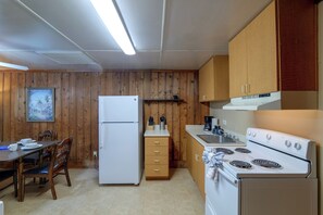 A compact kitchen with wooden walls, a refrigerator, a stove, and a dining area with a table and chairs. - Barefoot Getaway: Pool + Lake, 14 Mi to Disney (Clermont)