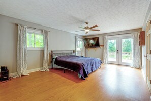 Ein Schlafzimmer mit Bett, Deckenventilator, Fernseher und einer Glastür zu einem Außenbereich.