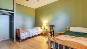 A room with two beds, a ceiling fan, a table with a lamp, and a chair.