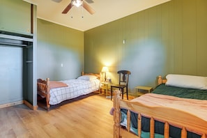 Een kamer met twee bedden, een plafondventilator, een tafel met een lamp en een stoel.