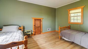 A room with two wooden beds, a window with blinds, a door, a radiator, and a ceiling fan.