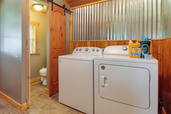 Een wasserette met twee witte Whirlpool wasmachines, een houten deur, een toilet en een metalen wand.