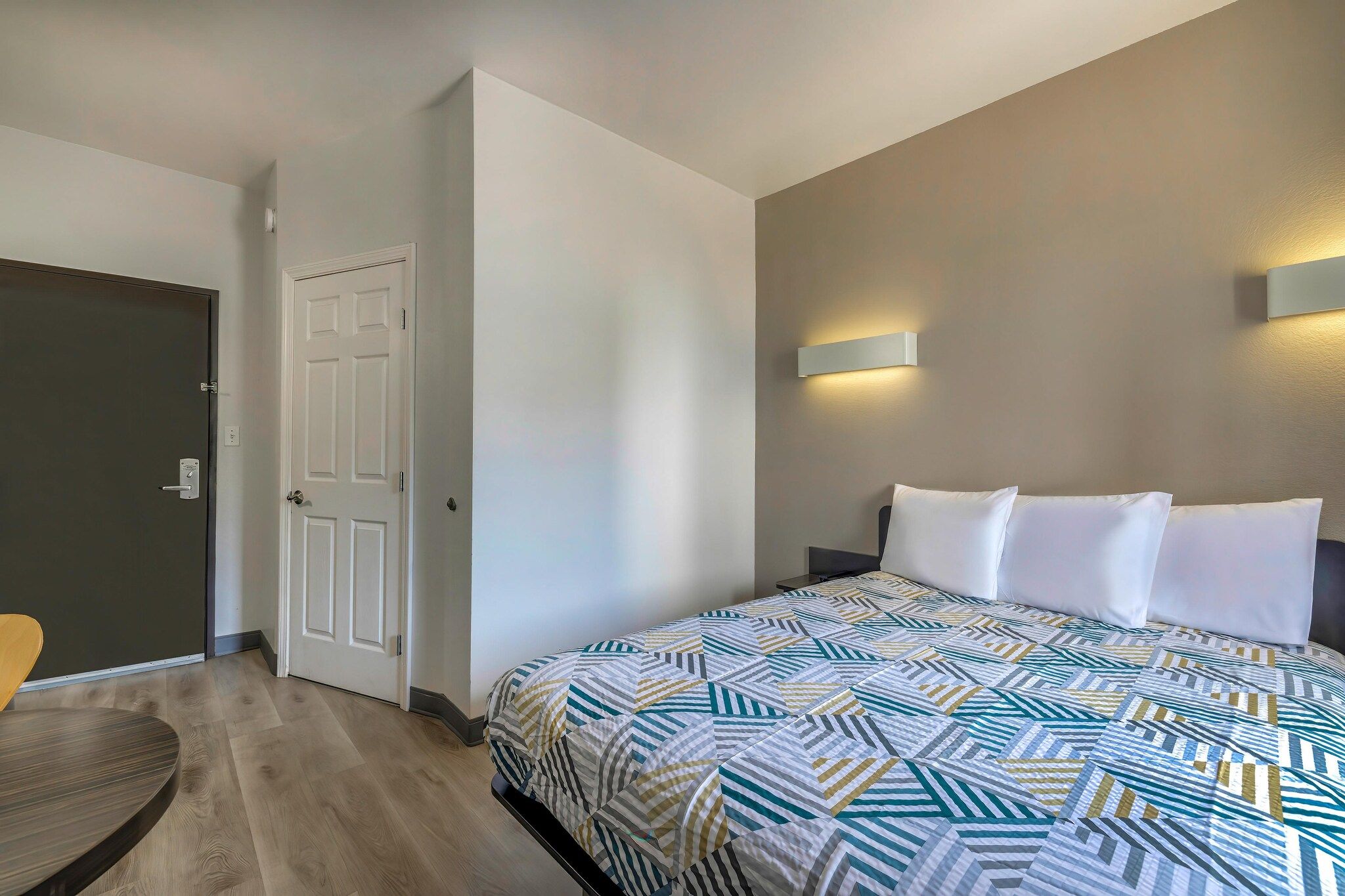 Une chambre d’hôtel avec un lit, une porte, une lampe fixée au mur et une chaise.