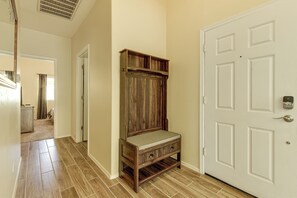 Un pasillo con un banco de madera, una puerta blanca y una rejilla de ventilación en el techo.