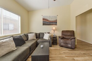 Una sala de estar con un sofá seccional, un sillón de cuero marrón, una mesita y una lámpara de pared.
