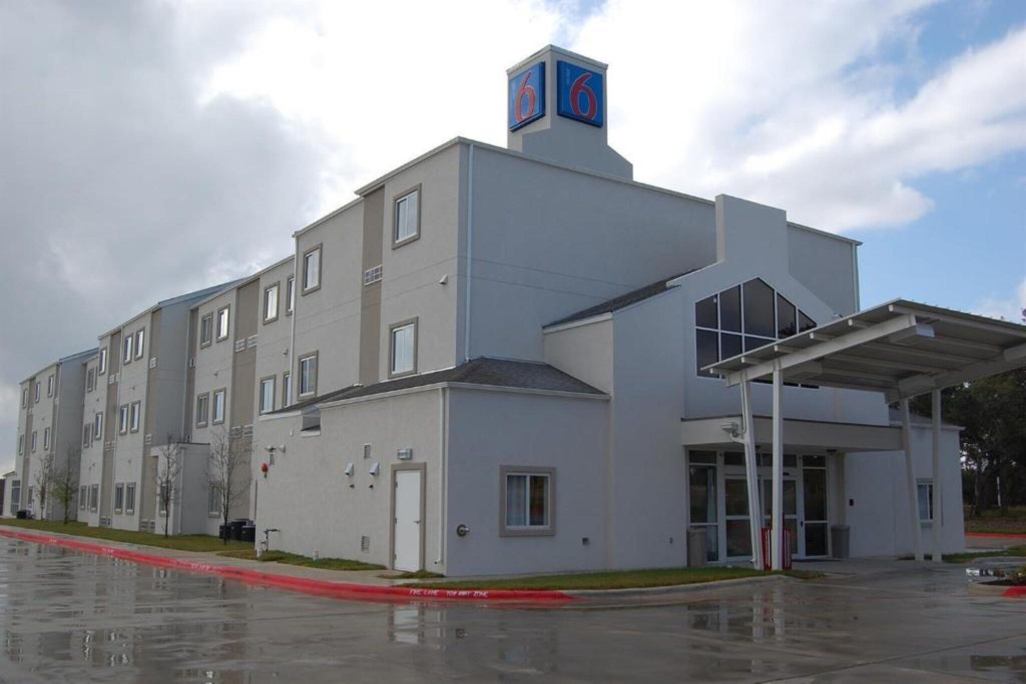 Un edificio de varios pisos con techo plano, un acceso cubierto y un letrero llamativo con el número '6'.