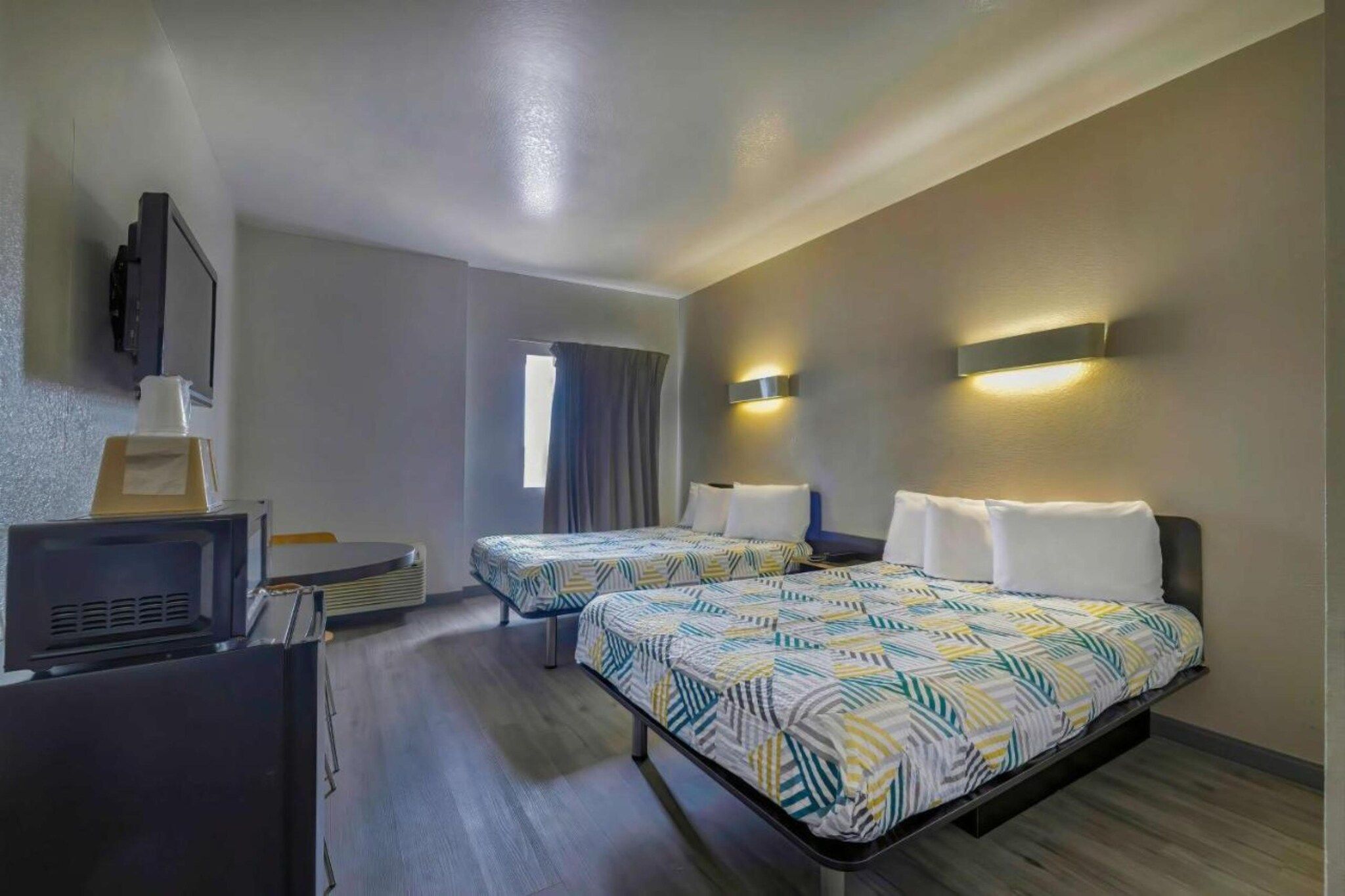 Ein Hotelzimmer mit zwei Betten, einem Fernseher, einem Schreibtisch und einem fensterbelagten Fenster.