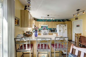 A kitchen with wooden cabinets, a central island, and a dining area with metal chairs. - Creekside New Castle Townhome w/ Scenic Deck (New Castle)