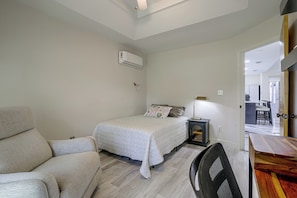 Ein Schlafzimmer mit einem Bett, einem Sessel, einem Standventilator und einer Klimaanlage an der Wand.