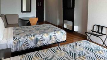 Habitación de hotel con dos camas, una silla, una mesita, un televisor y un espejo.