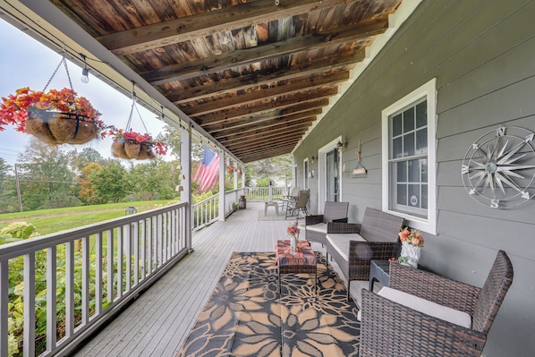 A covered porch with outdoor furniture, a decorative rug, and hanging flower baskets. - Retreat < 1 Mi to Otsego Lake & Opera’s House! (Cooperstown)
