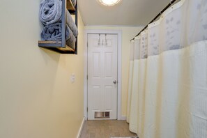 Un couloir avec une porte blanche, un porte-serviettes avec des serviettes pliées et un rideau de douche.